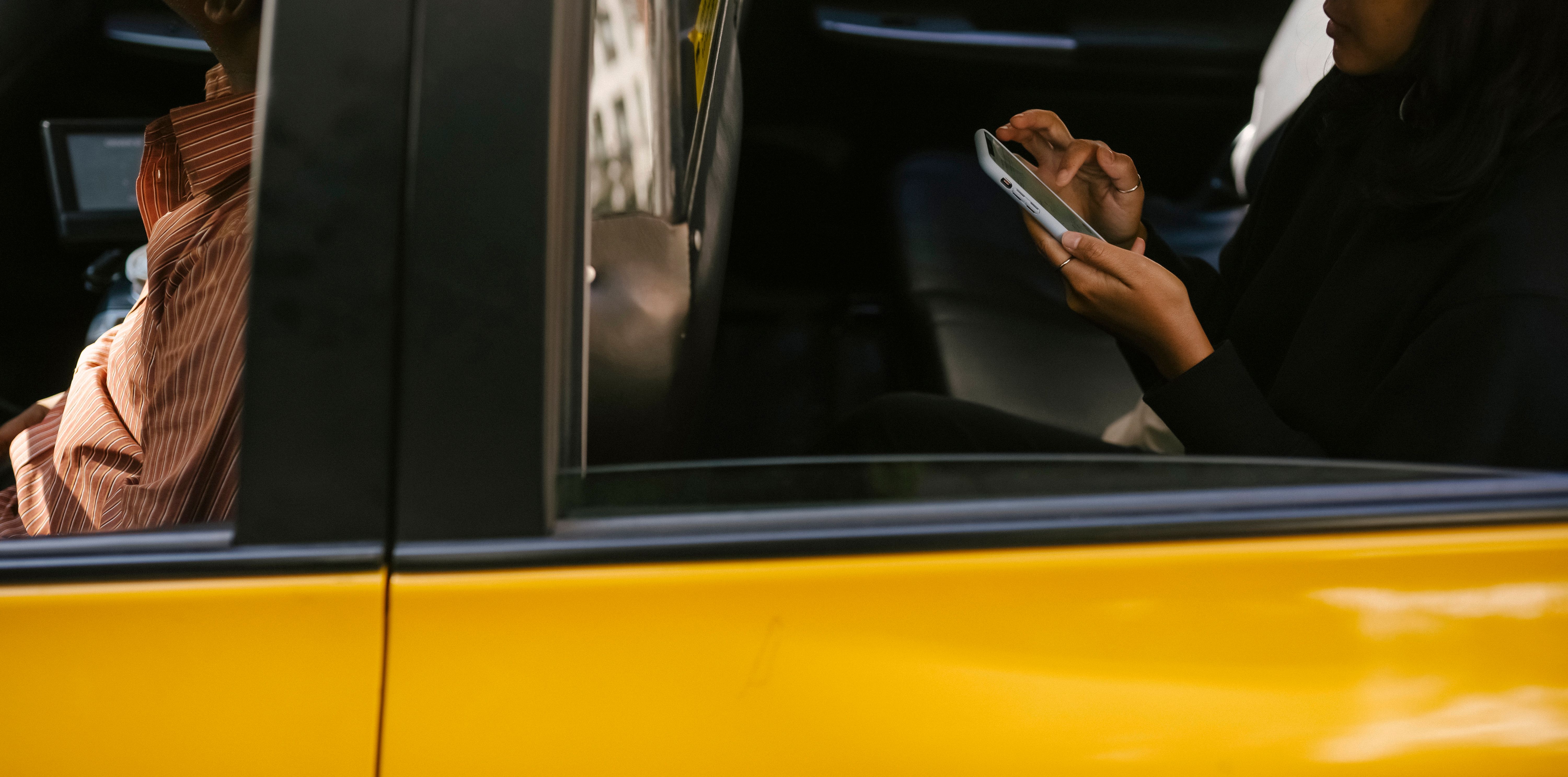 Passageira usando smartphone dentro de táxi amarelo — representação da experiência de transporte urbano profissional